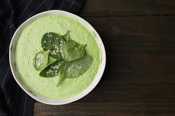 Delicious spinach cream soup with fresh leaves and sesame seeds in bowl on wooden table, top view. Space for text