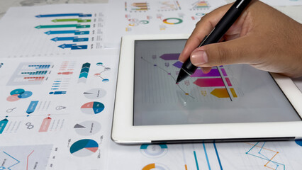 A persons hand uses a stylus to interact with a digital chart on a tablet. The tablet is laid on a...