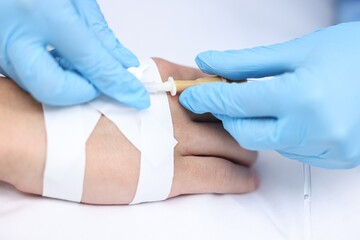 Nurse inserting IV into arm of patient in hospital, closeup