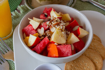a bowl of fruit salad containing diced apples and watermelon, garnished with almond slices. There are crackers on the side