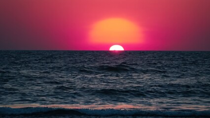 a photograph of the sun is setting over the ocean and the water is blue and pink in color