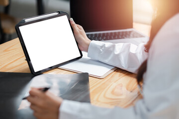 Business professional using a digital tablet at a desk with a laptop and documents in a modern office setting.
