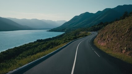 Fototapeta premium road going down a hill next to a body of water with mountains in the background