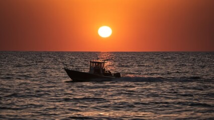 a photograph of the sun is setting over the ocean with a boat on the water in the foreground