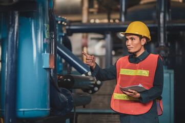 Asian engineer diligently inspects machinery in an industrial factory.Asian workers diligently...