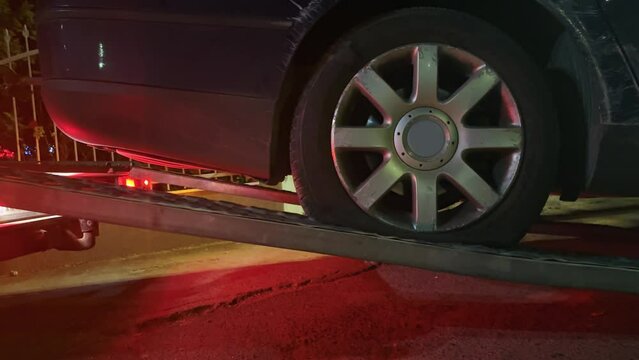 A black damaged car involved in accident is being towed by a tow truck ramp