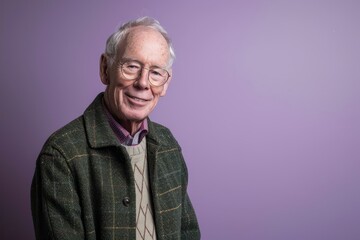 Obraz premium Portrait of a smiling senior man in a green jacket on a purple background.