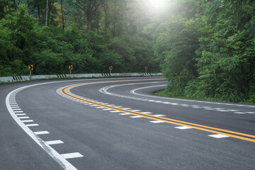Long curvy forest asphalt road over the hills. Beautiful curved road in the forest. Side view of road with fog at sunrise.