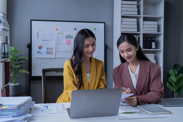 A professional photograph depicting two female entrepreneurs engaged in a collaborative discussion while diligently working in their corporate office environment.