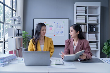 A professional photograph depicting two female entrepreneurs engaged in a collaborative discussion while diligently working in their corporate office environment.