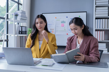 A professional photograph depicting two female entrepreneurs engaged in a collaborative discussion while diligently working in their corporate office environment.
