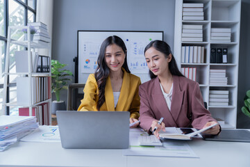 A professional photograph depicting two female entrepreneurs engaged in a collaborative discussion while diligently working in their corporate office environment.