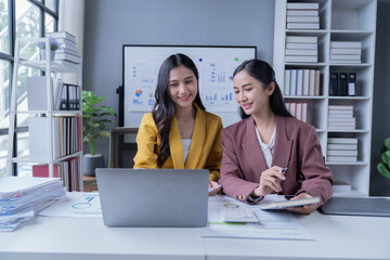 A professional photograph depicting two female entrepreneurs engaged in a collaborative discussion while diligently working in their corporate office environment.
