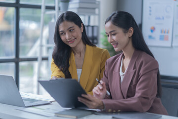 A professional photograph depicting two female entrepreneurs engaged in a collaborative discussion while diligently working in their corporate office environment.