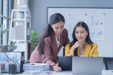 A professional photograph depicting two female entrepreneurs engaged in a collaborative discussion while diligently working in their corporate office environment.