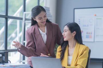 A professional photograph depicting two female entrepreneurs engaged in a collaborative discussion while diligently working in their corporate office environment.