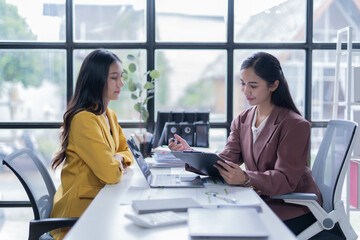A professional photograph depicting two female entrepreneurs engaged in a collaborative discussion while diligently working in their corporate office environment.