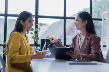 A professional photograph depicting two female entrepreneurs engaged in a collaborative discussion while diligently working in their corporate office environment.