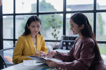 A professional photograph depicting two female entrepreneurs engaged in a collaborative discussion while diligently working in their corporate office environment.
