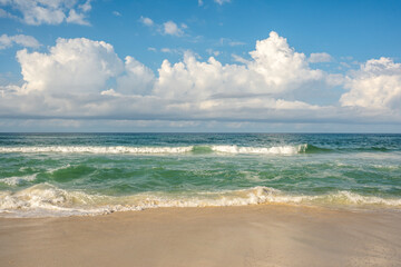 Photo of ocean waves crashing on a beautiful sandy beach with beautiful clouds in the blue sky.