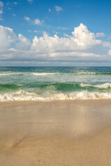 Photo of ocean waves crashing on a beautiful sandy beach with beautiful clouds in the blue sky.