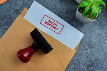Red Handle Rubber Stamper and Myth Busting text above brown envelope isolated on wooden background