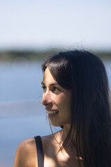 Woman in 20s smiling and looking happy in front of ocean 