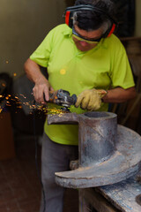 A man in a green shirt is working on a piece of metal with a grinding tool. Concept of hard work and dedication, as the man is focused on his task