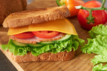 Sandwich with ham, cheese and vegetables on a wooden board.