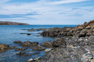 A picturesque view over Ha Ha Bay from the rugged Back Cove in Raleigh, situated at the northern tip of Newfoundland's Great Northern Peninsula, featuring the remains of an iceberg in the distance.
