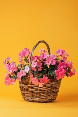 A basket full of pink flowers sits on a yellow background. The basket is made of wicker and is filled with a variety of pink flowers. The flowers are arranged in a way that creates a sense of harmony
