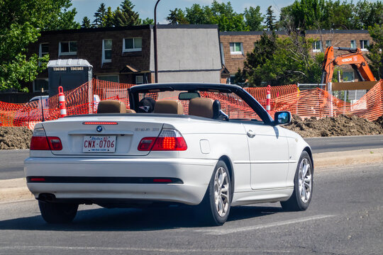 Calgary, Alberta, Canada. Jun 25, 2024.A white convertible with a black top driving on a city street next to a construction zone. The 2001 BMW 325Ci, a popular two-door model vehicle.