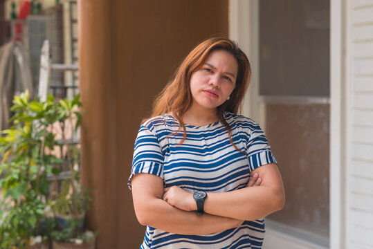 An Asian woman in her 30s stands outside her apartment flat, looking at someone with a suspicious and condescending expression. Annoyed at her intelligence being insulted.