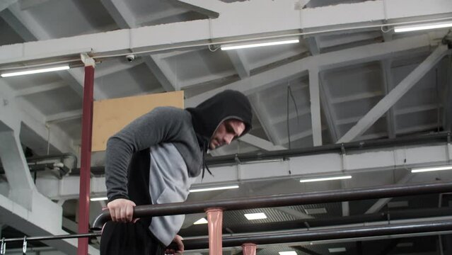 Determined male athlete doing dibs on parallel bars. Sportsman wearing hooded iacket exercising at gym. He is performing muscle training at healthcare centre. 