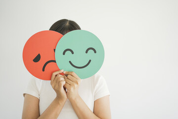 Woman hands holding sad face hiding behind happy face, bipolar and depression, mental health, split personality, mood change concept