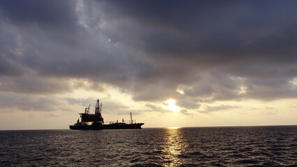 Drilling rig and FPSO ship or floating processing storage offloading ship silhouette view in sunset offshore background