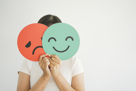 Woman hands holding sad face hiding behind happy face, bipolar and depression, mental health, split personality, mood change concept