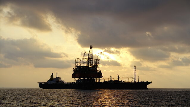 Drilling rig and FPSO ship or floating processing storage offloading ship silhouette view in sunset offshore background