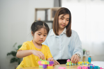 Asian woman and a child are playing with blocks. The woman is helping the child build a tower