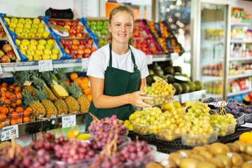 Young salesgirl at her first job, selling green grape and other fruits in vegetable shop
