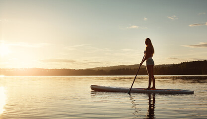 Lake, sunshine and woman on paddle board for water sport, forest and vacation on river for tourism. Exercise, woods or holiday in Germany for female person, swimsuit or travel fitness for adventure