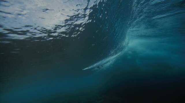 Underwater sideview of surfer riding and carving into top of wave at Cloudbreak Fiji