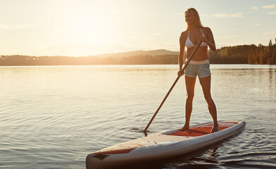 Lake, sunset and woman on paddle board for exercise, water sport and vacation on river for tourism. Sunshine, summer and holiday in Germany for female person, swimsuit or travel fitness for adventure