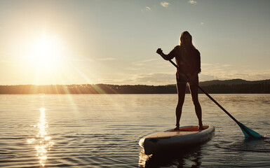 Lake, sunset and woman on paddle board for relax, water sports and vacation on river for tourism. Sunlight, summer and holiday in Germany for female person with silhouette, swimsuit and travel
