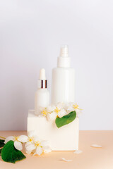 Cosmetic toner and serum in blank packages on a podium against a white wall background with jasmine flowers. Natural skin care products concept