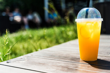 Orange lemonade with ice in a glass on the street. Summer citrus refreshing drink