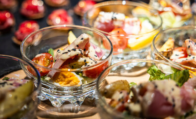 Close-up of small glass bowls filled with salad, featuring tomatoes, lettuce, egg, and a creamy dressing topped with sesame seeds. The bowls are arranged on a wooden surface.