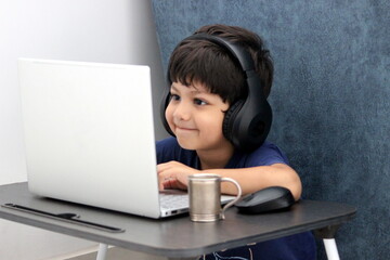 cute boy is e-learning on laptop. he is smiling while interacting with his teacher online. he is expressive and communicating over the conference call. distance learning is great tool for kids growth.