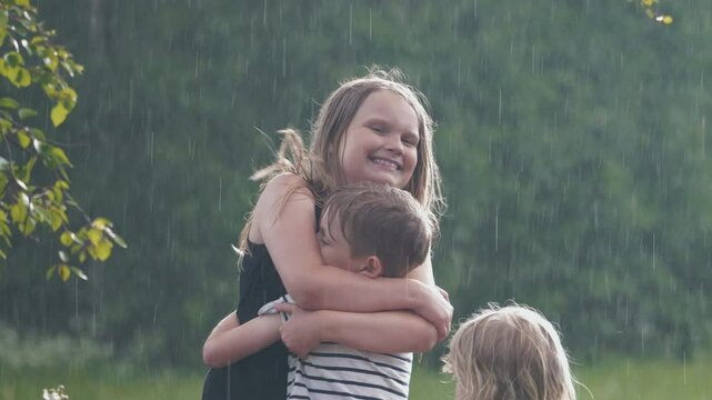 Happy sibling hugging and smiling in summer rain. Slow motion