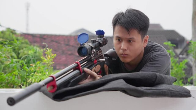 Asian sniper flips up lens cap covers on scoped pcp air rifle looking and aiming
